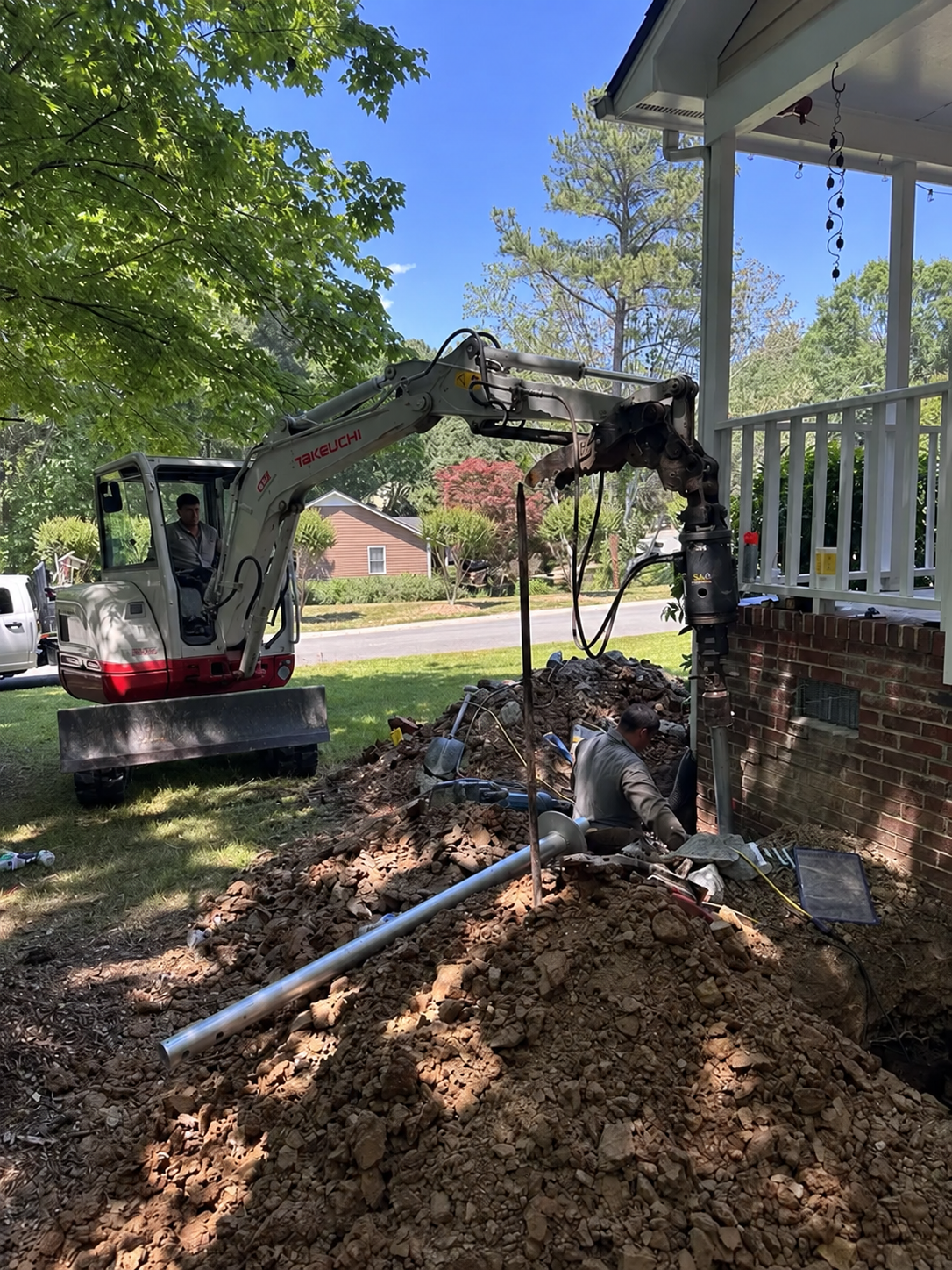 Foundation repair crew excavating beside a brick home